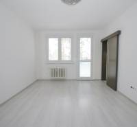 A spacious white room with a wood-patterned floor and a large window in a 3-room apartment.