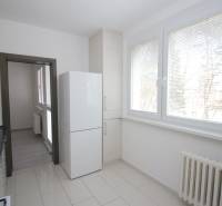 A kitchen in a 3-room apartment with large windows, a refrigerator, and light-colored tiles.