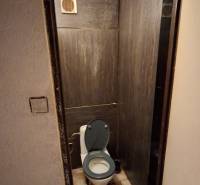 A toilet with tiles in a 3-room apartment, dark tiles on the walls.