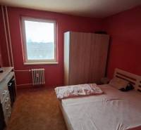 A bedroom in a 3-room apartment with a bed, wardrobe, and dresser on a red wall.