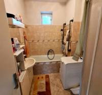 Bathroom with a bathtub, sink, washing machine, and shelves in a family house.