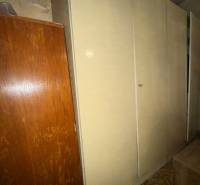 A wardrobe in a family house, next to it is brown furniture and a carpet with a geometric pattern.