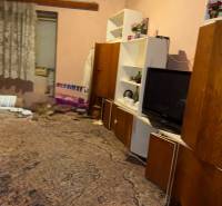 A room in a family house with a carpet, shelves, a television, and curtains.