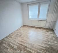 An empty room with white walls and a wooden-patterned floor in a three-room apartment.