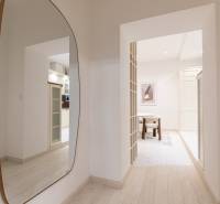 A hallway with a mirror and a view into the kitchen in a 3-room apartment with a wooden decor floor.