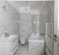A bathroom with marble decor walls, a bathtub, and a sink in a 2-room apartment.
