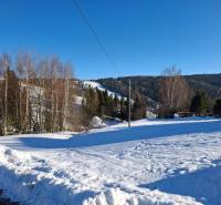 Snow-covered residential plots in Ždiar, surrounded by forests and mountains.