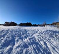 Snow-covered lands in Ždiar with visible houses in the background, clear blue sky.
