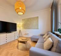 Living room in a two-room apartment with a wooden decor floor, a sofa, and a TV.