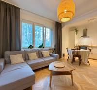 Living room with kitchen and dining table, wooden decor flooring, light-colored sofa.