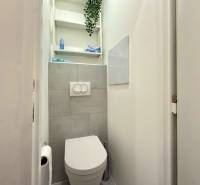 Bathroom in a 2-room apartment with a toilet, white walls, and shelves.