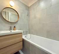 Bathroom with a bathtub in a 2-room apartment, a mirror, and a backlit washbasin cabinet.
