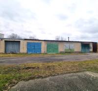 A building with a series of colorful garage doors in Kuklov, next to an asphalt road.