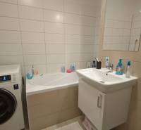 A bathroom with a bathtub, washing machine, and sink in a 2-room apartment.