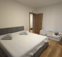 Bedroom with a gray bed and a baby crib, wooden decor flooring in a 2-room apartment.