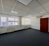 An office with carpeted flooring, white walls, air conditioning, and vertical blinds on the windows.