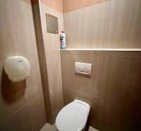 A restroom with tiles in an office, with a cleaning product and a toilet paper dispenser.