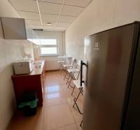 A narrow kitchenette with linoleum flooring, a refrigerator, and a window in office spaces.