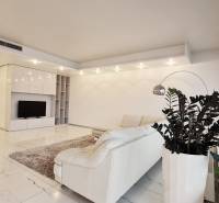 Living room in a 3-room apartment with a white couch, plants, and a TV on a light floor.