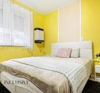 Bedroom in a family house with yellow walls, a white bed, and floral decoration.