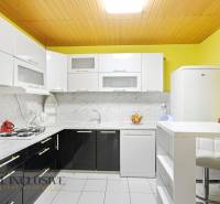 A kitchen in a family house with light cabinets, marble tiles, and white appliances.