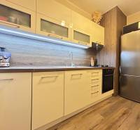 A kitchen in a 2-room apartment with a wooden decor floor, built-in appliances, and storage cabinets.