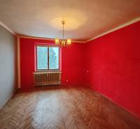 A room with red walls, a chandelier, and a wooden decor floor in a two-room apartment.