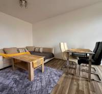 Living room of a three-room apartment with a sofa, table, and wood-patterned floor.