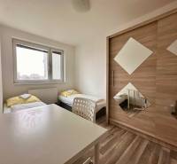 A bedroom with two beds, a white table, and a wardrobe in a three-room apartment.