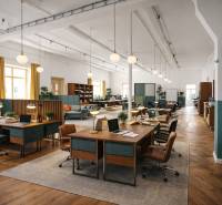 Interior of a building with office desks, chairs, wood-patterned flooring, and lighting.