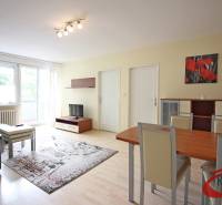 Living room in a three-room apartment with a wooden decor floor, a sofa, and a dining table.