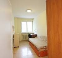 A narrow room with a bed, a table, and a wardrobe, a floor with a wooden decor in a 3-room apartment.
