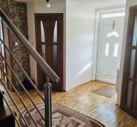 A hallway of a family house with a wooden decor floor and a staircase with a metal railing.