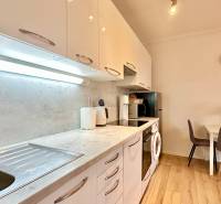 A kitchen in a 2-room apartment with a wooden decor floor, a dining table, and appliances.