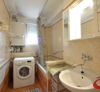A bathroom with a bathtub and a washing machine in a 3-room apartment, with cream-colored tiles.