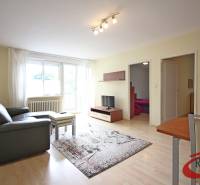 Living room of a three-room apartment with a sofa, table, and television on a wooden-decor floor.