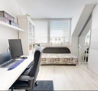 Home office in a family house with a desk and a bed, floor with wooden decor.