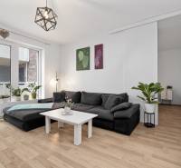 Living room in a 3-room apartment with a large couch, plants, and a floor with a wood decor.