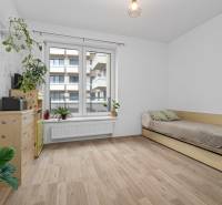 A room in a 3-room apartment with a wooden decor floor, a bed, and plants.