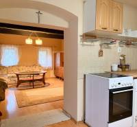 A kitchen and living room in a cottage with a wooden decor floor, a comfortable sofa, and a stove.