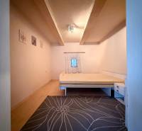 A simply furnished room in a cottage with carpet and wood-patterned flooring.