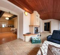 A cottage with a fireplace and a wooden decor floor, connected to the dining room and kitchen.