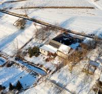 A snowy landscape with a cottage on Zánemecká Street in Hriňová, surrounded by fields and roads.