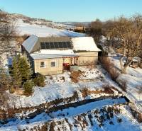 A cottage on Zánemecká Street in Hriňová, surrounded by a snowy hilly landscape with solar panels.