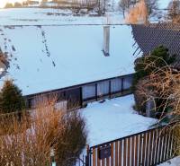 A cottage in a snowy landscape on Zánemecká Street in Hriňová, surrounded by trees.