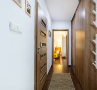 A hallway of a 3-room apartment with a wooden decor floor, wooden doors, and a yellow armchair.