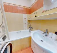Bathroom with a sink, bathtub, and washing machine in a 3-room apartment. Beige and orange tiles.