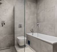 A bathroom with a bathtub and shower in a 3-room apartment, tiled with gray tiles.