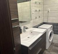 A bathroom in a 3-room apartment with a sink, washing machine, and mirrored wall.