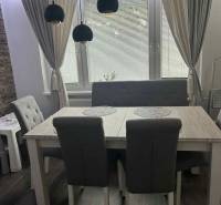 Dining area in a 3-room apartment with dark flooring and curtains, gray furniture.
